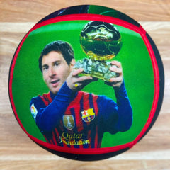 A round soccer ball featuring a printed graphic of Lionel Messi holding the FIFA World Cup trophy, with a green background, red trim, and FC Barcelona branding.