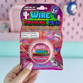 Wire Drawing Mud packaging held by a hand with a pink background