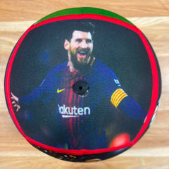 A round decorative pillow featuring a printed graphic of soccer player Lionel Messi in a blue FC Barcelona jersey, with a red and green border, photographed on a light wood floor.