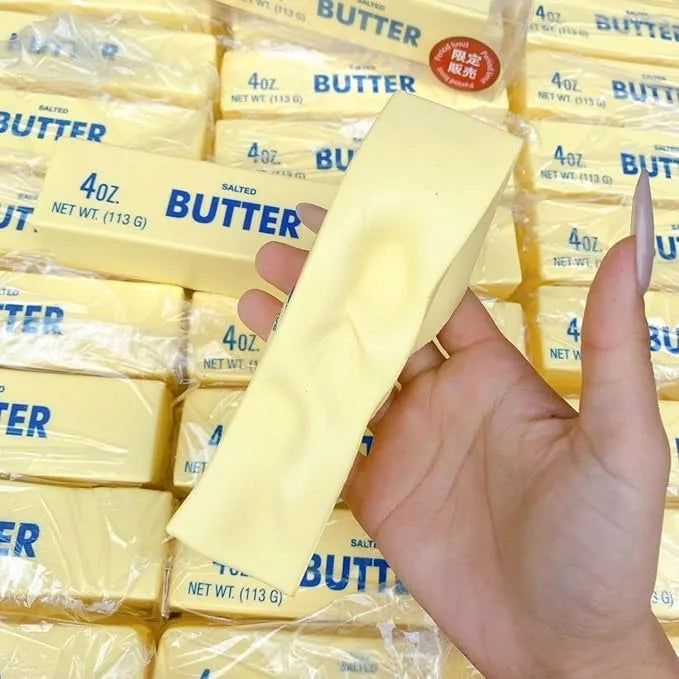 A hand holding a stick of pale yellow salted butter in front of a stacked background of packaged butter sticks.