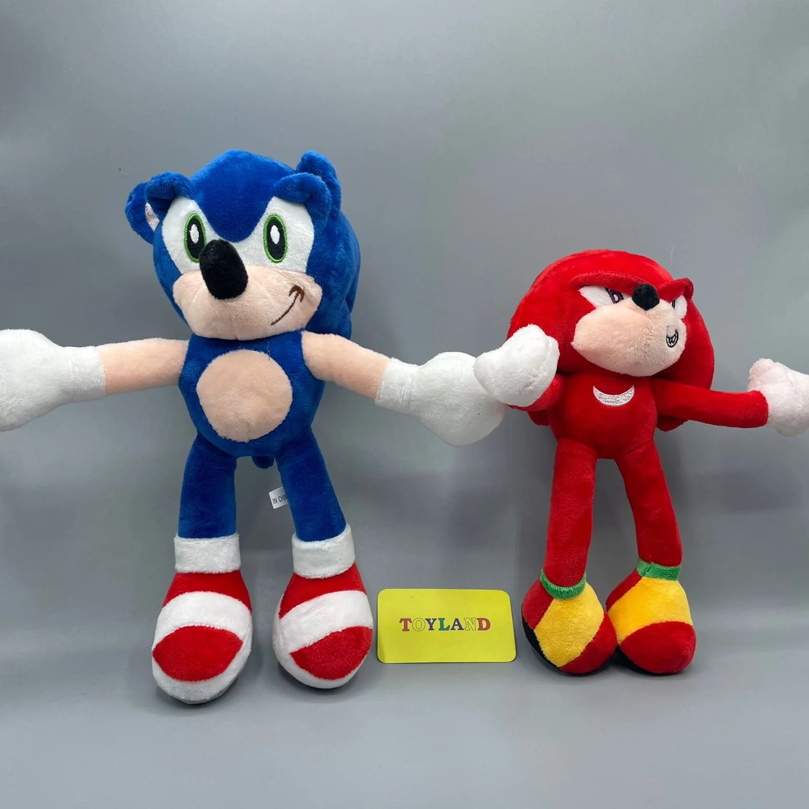 Two plush toys, one blue and one red, holding hands with a 'Toyland' label below on a gray background.