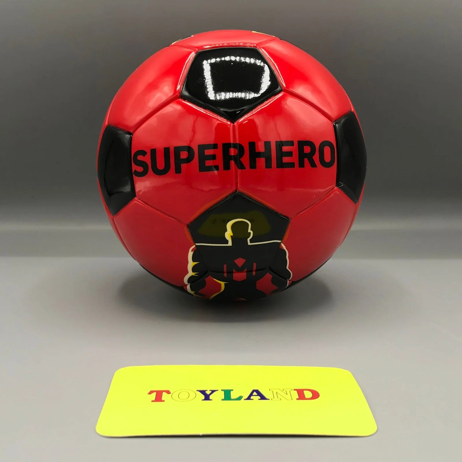 Red soccer ball with 'Superhero' text and silhouette on a gray background, featuring a 'Toyland' card.