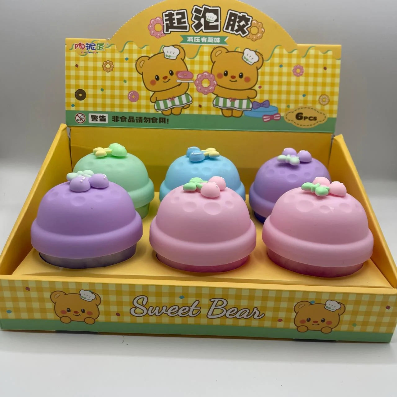 Set of colorful bell-shaped toys with a 'Sweet Bear' branded box on a gray background
