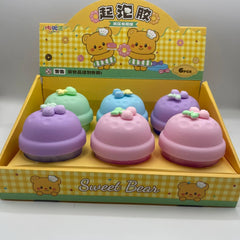 Set of colorful bell-shaped toys with a 'Sweet Bear' branded box on a gray background